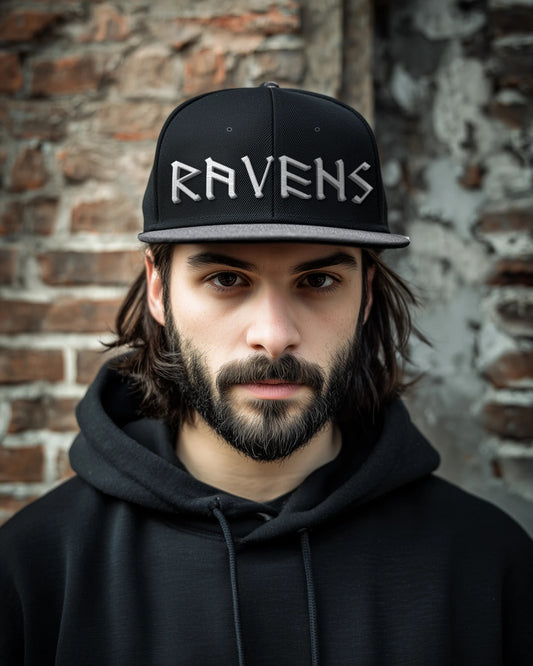 Mann trägt die Ravens Snapback in Schwarz/Silber mit 3D-Puff-Stickerei RAVENS vor einer Backsteinwand